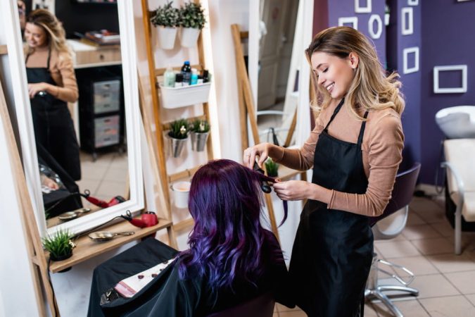 Coiffeuse souriante réalisant des boucles sur des cheveux violets, une source d'inspiration pour ouvrir un salon de coiffure créatif