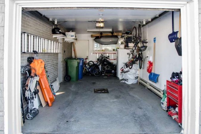 Garage encombré avec vélos suspendus, moto, poubelles et outils rangés contre les murs, illustrant la nécessité d'organiser son garage efficacement.