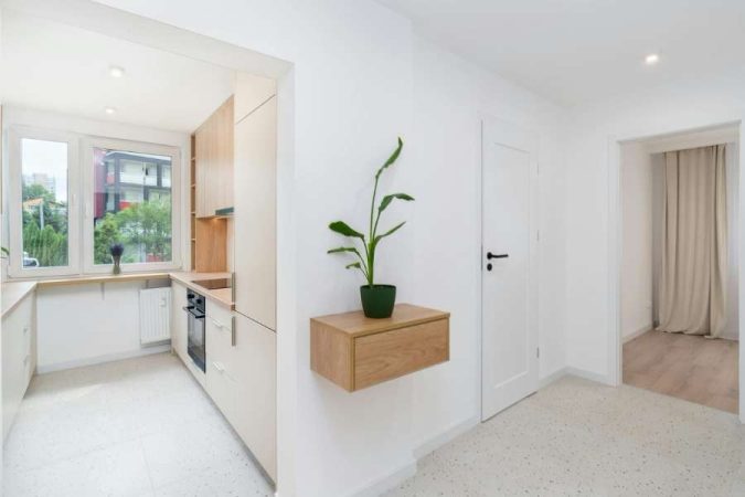 Une cuisine ouverte blanche et bois clair avec une plante verte en pot sur une étagère murale suspendue, intégrée harmonieusement dans la décoration intérieure.