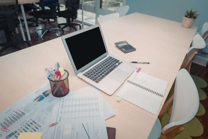 Un bureau en bois clair ordonné avec un ordinateur portable ouvert, une calculatrice et des documents analytiques imprimés.